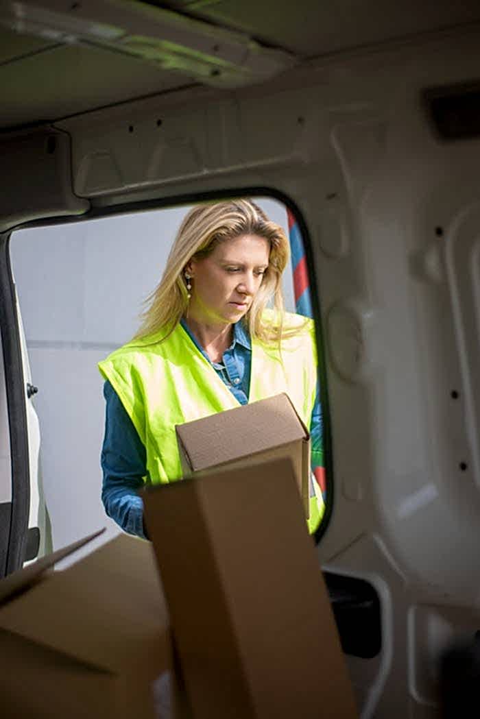 Woman in high-visibility vest loading packages inside a delivery van.